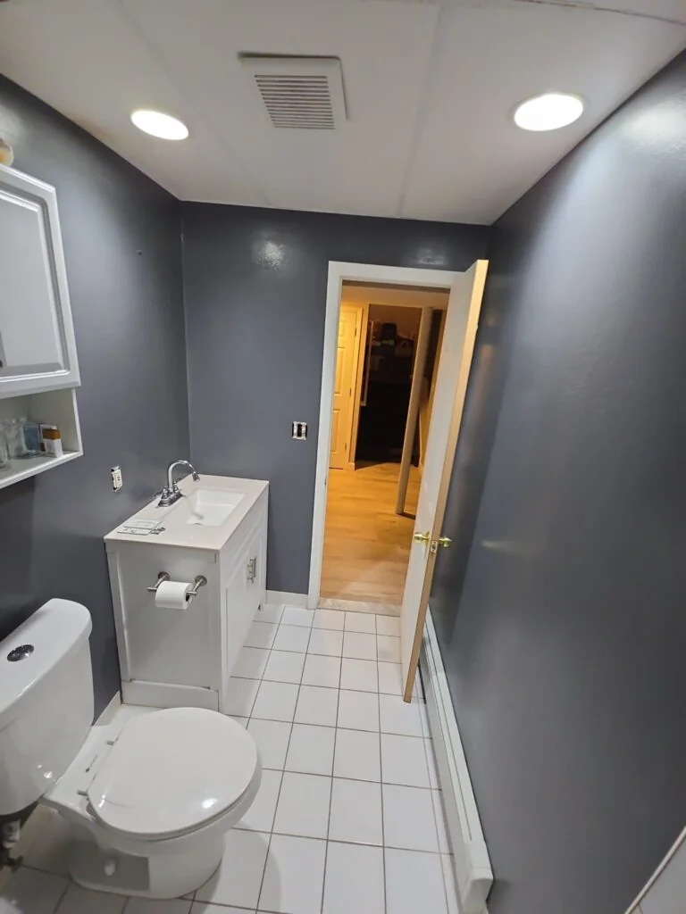 Compact bathroom with gray walls, white tile, toilet, and vanity